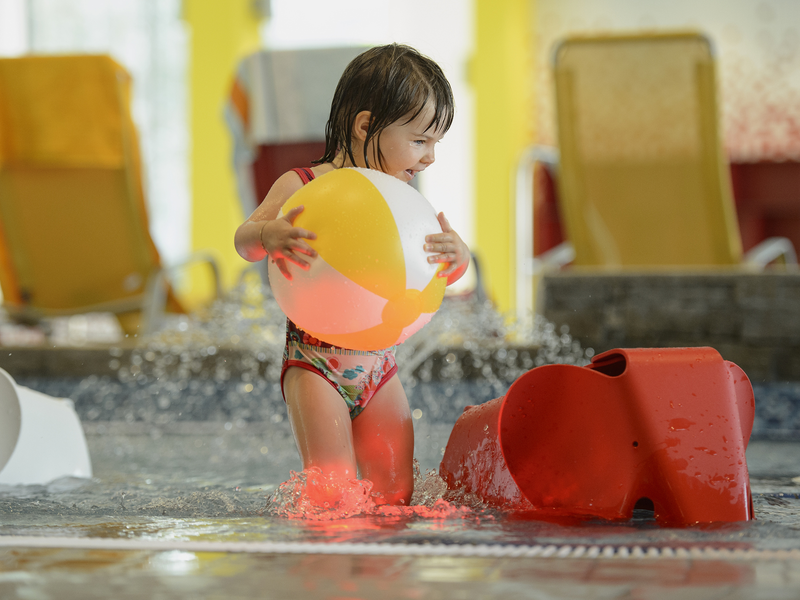 Kind spielt mit einem Wasserball im Kinderbecken