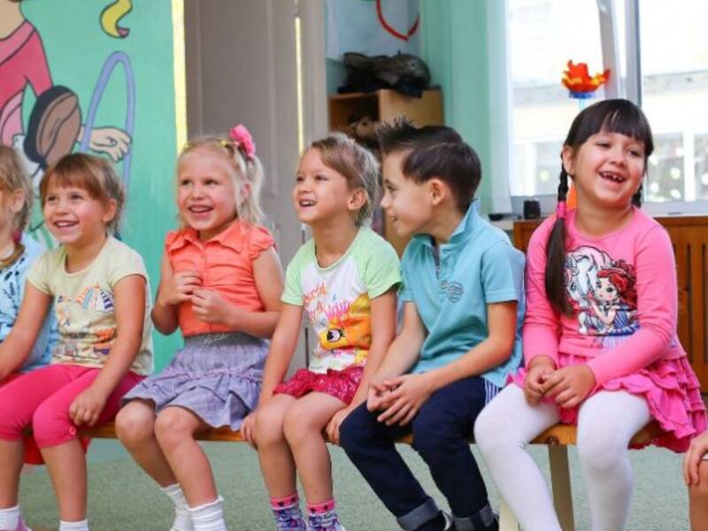 Fünf lachende Kinder sitzen auf einer Bank im Kidnergarten