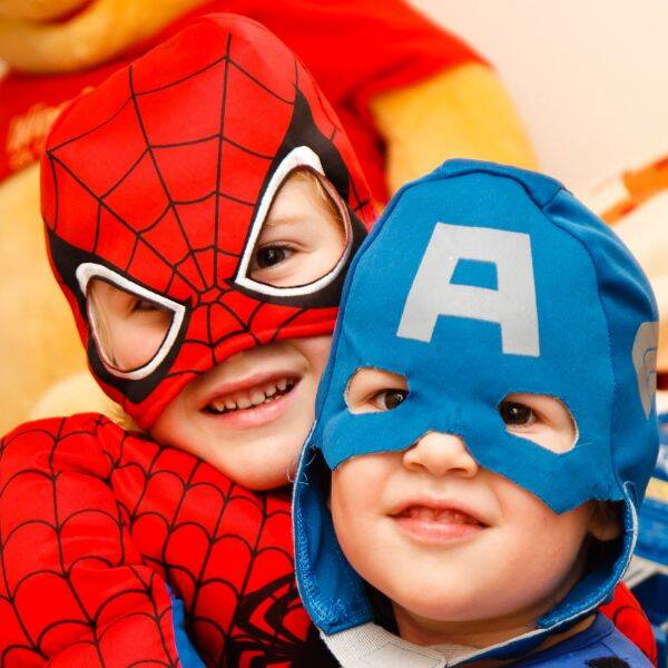 Zwei Kinder sind verkleidet. Das eine trägt ein Spider-Man Kostüm und das andere eine blaue Maske mit einem großen A drauf.