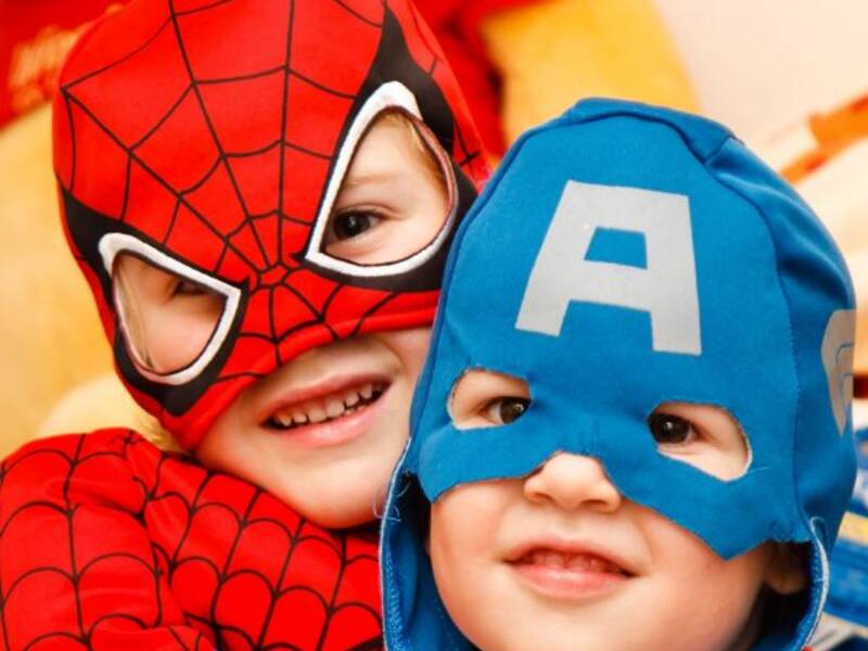 Zwei Kinder sind verkleidet. Das eine trägt ein Spider-Man Kostüm und das andere eine blaue Maske mit einem großen A drauf.