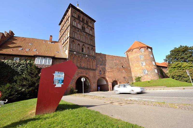 Eingang einer Burg mit einem Auto im Vordergrund und einer Informationstafel daneben.