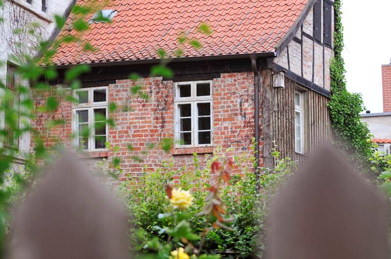 Ein Haus mit Klinker-Steinen in Rot. Davor die Spitzen eines Lattenzauns in unscharf.