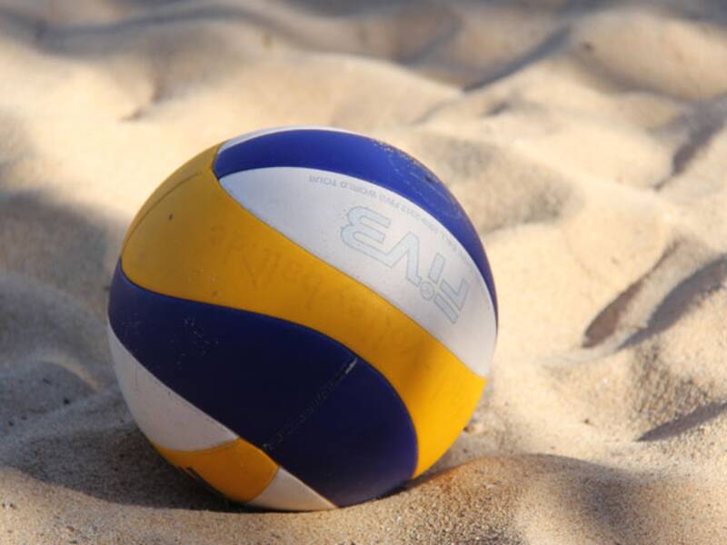 Volleyball in den Farben Gelb, Weiß und Blau. Der Ball liegt im Sand. .