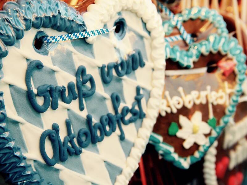 Herz aus Süßigkeiten von dem Oktoberfest. Das Herz ist in den Farben Blau und Weiß. Im Hintergrund hängen noch weitere Herzen in diesem Stil.