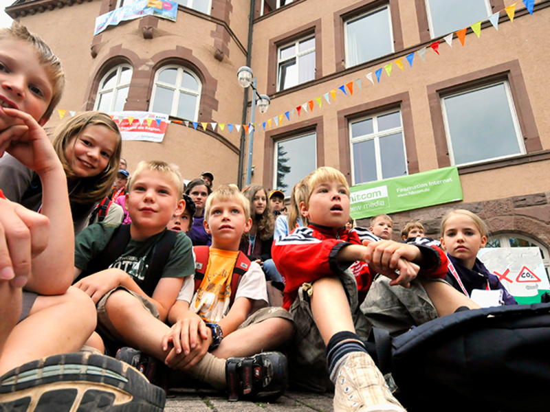 Kinder sitzen auf dem Schulhof auf dem Boden und schauen nach vorne